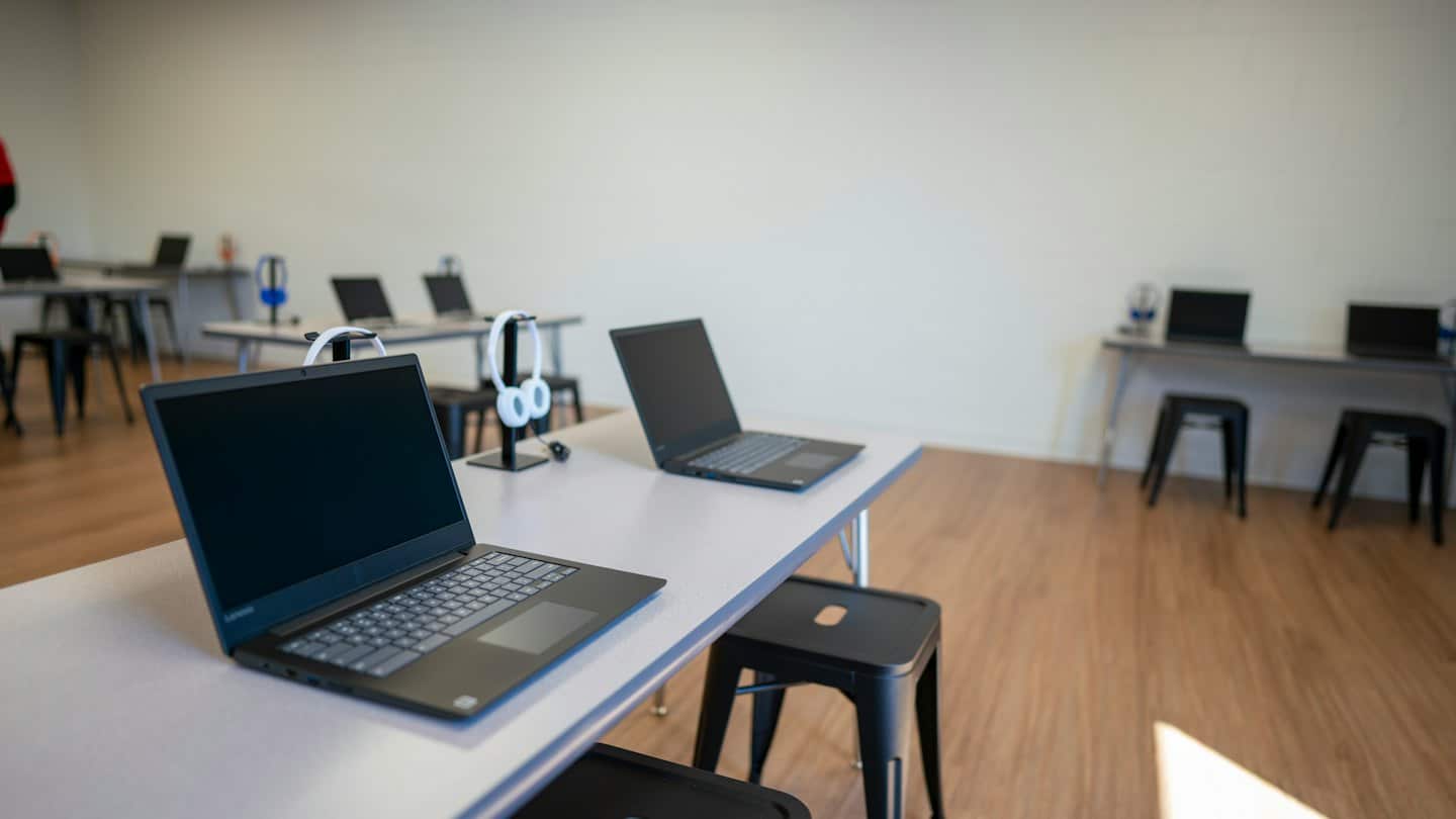 Tomt modernt klassrum med laptops och hörlurar på skrivborden.