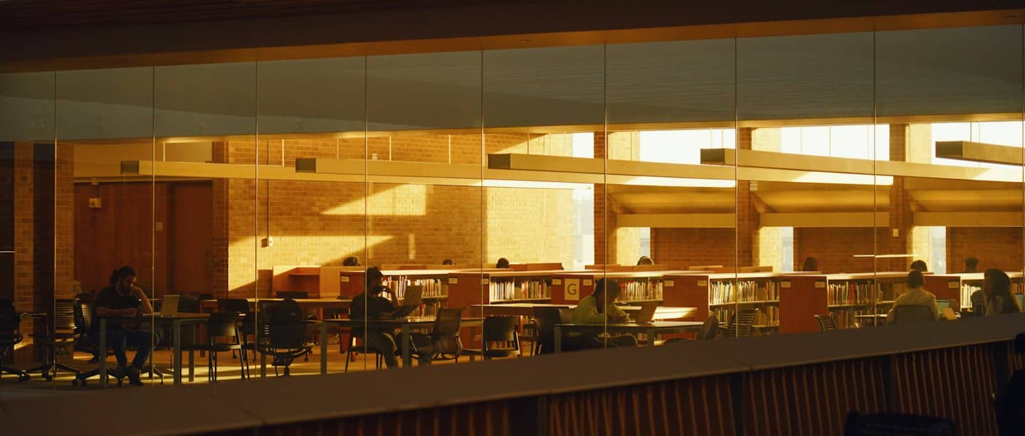 Studenter arbetar på bärbara datorer i ett soligt universitetsstudieområde.